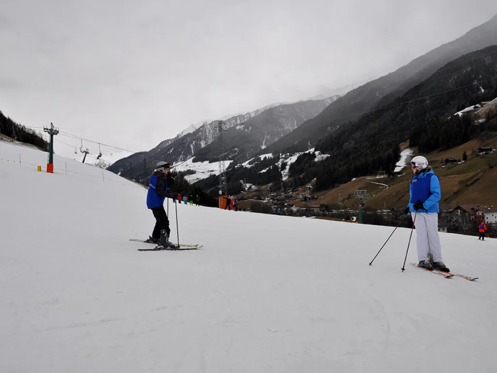Zwei Skifahrende auf der Piste vor einem nebligen Talhang.